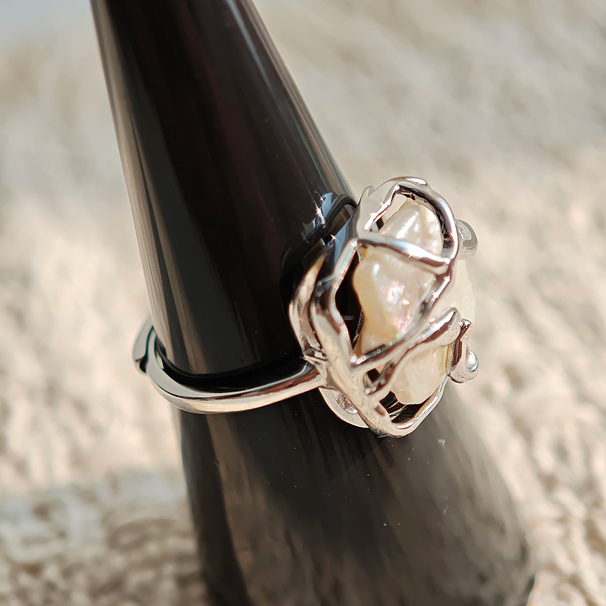 This adjustable S925 sterling silver ring features a striking baroque pearl at its center, set within an organic, flowing silver frame that wraps around the irregular, lustrous gemstone. The open, sculptural metalwork creates a modern, artistic silhouette, showcasing the pearl's natural, one-of-a-kind texture and soft iridescence. The sleek, polished silver band complements the unique pearl, making it a standout piece with a contemporary, bohemian aesthetic.