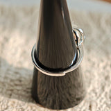 This adjustable S925 sterling silver ring features a striking baroque pearl at its center, set within an organic, flowing silver frame that wraps around the irregular, lustrous gemstone. The open, sculptural metalwork creates a modern, artistic silhouette, showcasing the pearl's natural, one-of-a-kind texture and soft iridescence. The sleek, polished silver band complements the unique pearl, making it a standout piece with a contemporary, bohemian aesthetic.