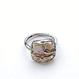 This adjustable S925 sterling silver ring features a striking baroque pearl at its center, set within an organic, flowing silver frame that wraps around the irregular, lustrous gemstone. The open, sculptural metalwork creates a modern, artistic silhouette, showcasing the pearl's natural, one-of-a-kind texture and soft iridescence. The sleek, polished silver band complements the unique pearl, making it a standout piece with a contemporary, bohemian aesthetic.