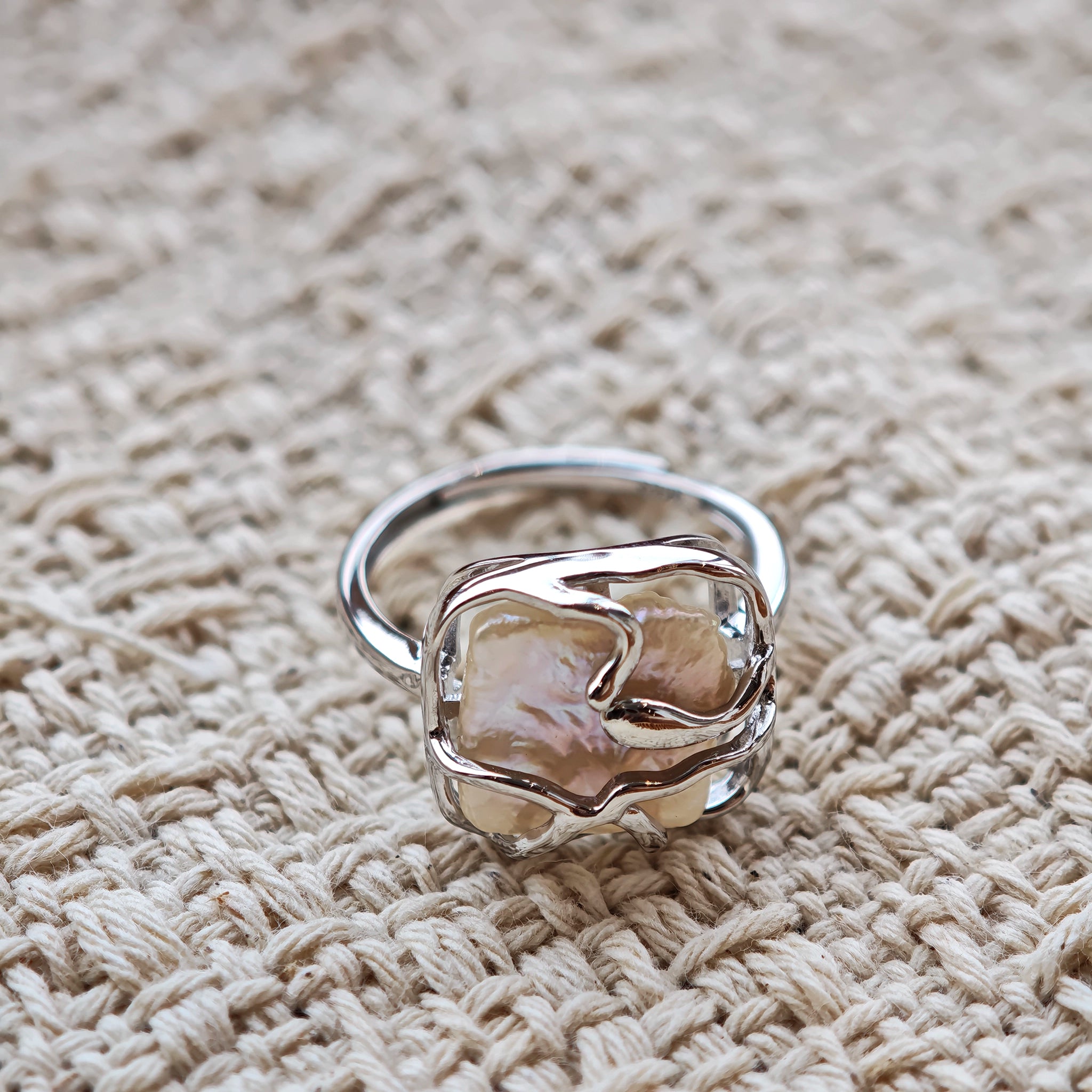 This adjustable S925 sterling silver ring features a striking baroque pearl at its center, set within an organic, flowing silver frame that wraps around the irregular, lustrous gemstone. The open, sculptural metalwork creates a modern, artistic silhouette, showcasing the pearl's natural, one-of-a-kind texture and soft iridescence. The sleek, polished silver band complements the unique pearl, making it a standout piece with a contemporary, bohemian aesthetic.