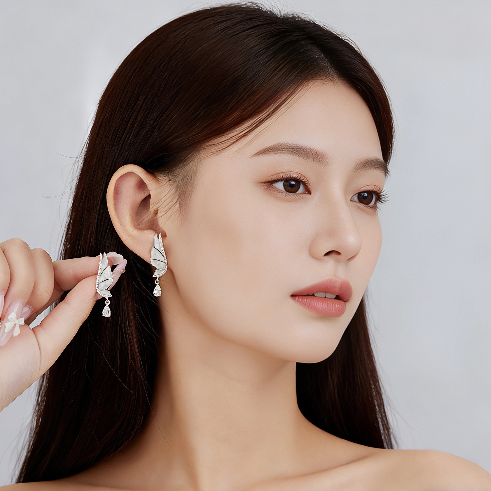 These S925 sterling silver earrings are designed in the shape of delicate butterfly wings, with a resin craft on the wing surfaces and a row of shimmering cubic zirconia along the edges. A teardrop-cut clear gemstone dangles elegantly from the bottom of each wing, adding a graceful and sparkling touch to the overall design.