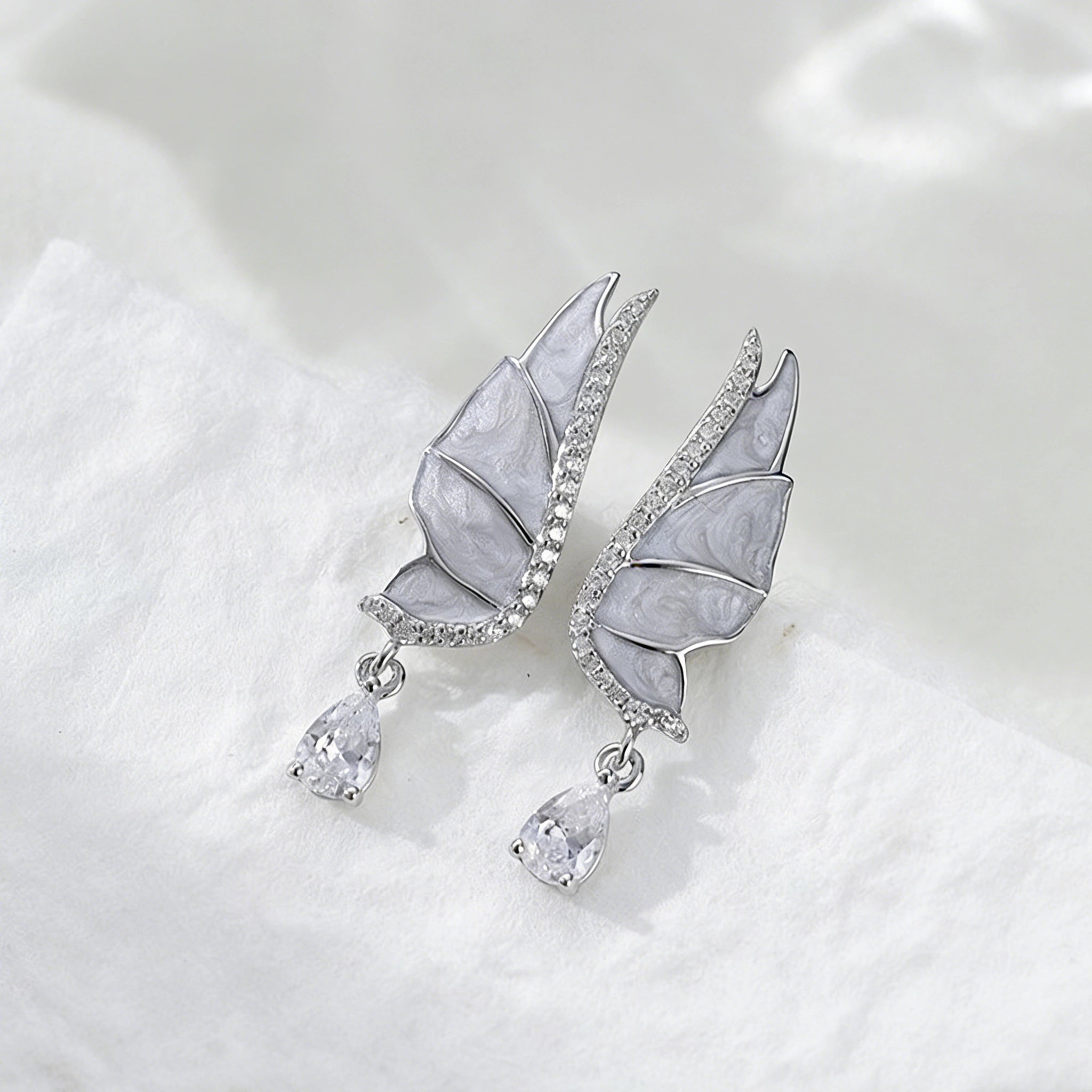 These S925 sterling silver earrings are designed in the shape of delicate butterfly wings, with a resin craft on the wing surfaces and a row of shimmering cubic zirconia along the edges. A teardrop-cut clear gemstone dangles elegantly from the bottom of each wing, adding a graceful and sparkling touch to the overall design.