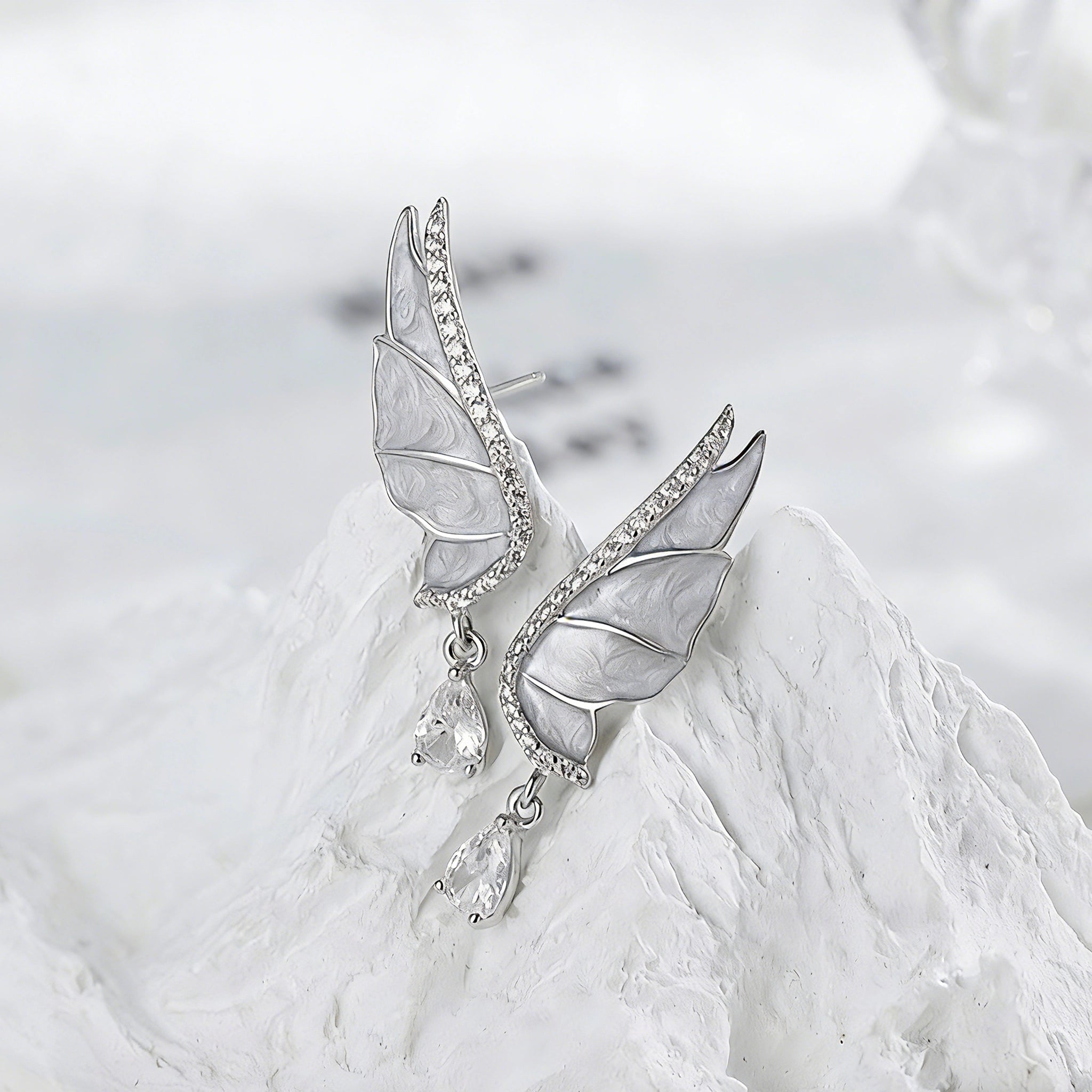 These S925 sterling silver earrings are designed in the shape of delicate butterfly wings, with a resin craft on the wing surfaces and a row of shimmering cubic zirconia along the edges. A teardrop-cut clear gemstone dangles elegantly from the bottom of each wing, adding a graceful and sparkling touch to the overall design.