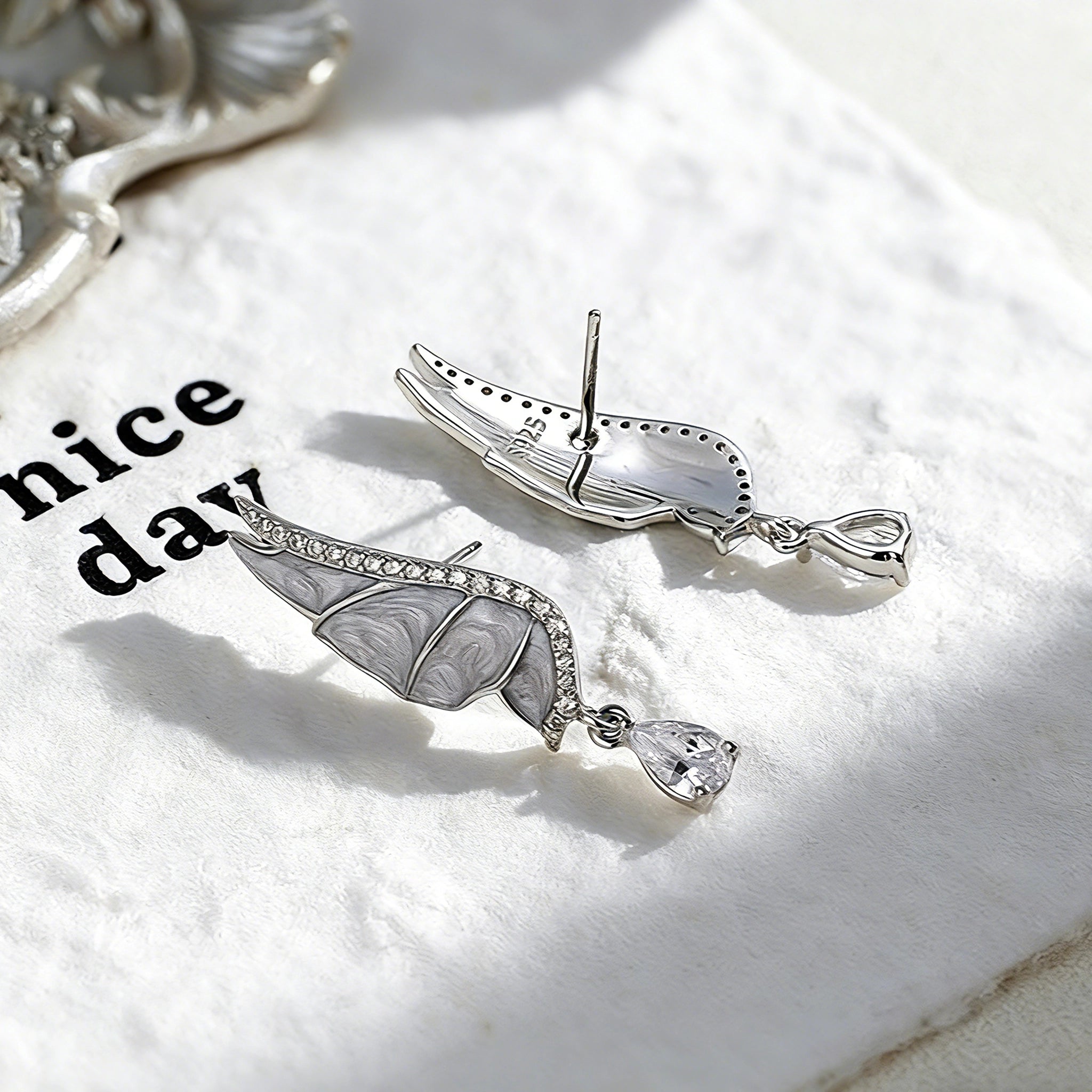 These S925 sterling silver earrings are designed in the shape of delicate butterfly wings, with a resin craft on the wing surfaces and a row of shimmering cubic zirconia along the edges. A teardrop-cut clear gemstone dangles elegantly from the bottom of each wing, adding a graceful and sparkling touch to the overall design.