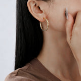 These S925 sterling silver hoop earrings feature a textured, molten lava-like finish in a warm gold tone. The organic, uneven surface creates a rugged, handcrafted appearance, while the classic oval hoop shape adds a timeless, elegant touch to the design. The secure post-back closure ensures comfortable all-day wear.