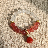 This bracelet features a beautiful blend of translucent white phantom quartz beads and rich pink strawberry quartz beads, creating a striking contrast. Adorned with delicate gold-toned accents and a charming red cat's paw charm, it exudes a sweet and elegant vibe. The combination of smooth crystal spheres and a playful pendant makes it a lovely and eye-catching accessory.