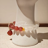 This bracelet features a beautiful blend of translucent white phantom quartz beads and rich pink strawberry quartz beads, creating a striking contrast. Adorned with delicate gold-toned accents and a charming red cat's paw charm, it exudes a sweet and elegant vibe. The combination of smooth crystal spheres and a playful pendant makes it a lovely and eye-catching accessory.