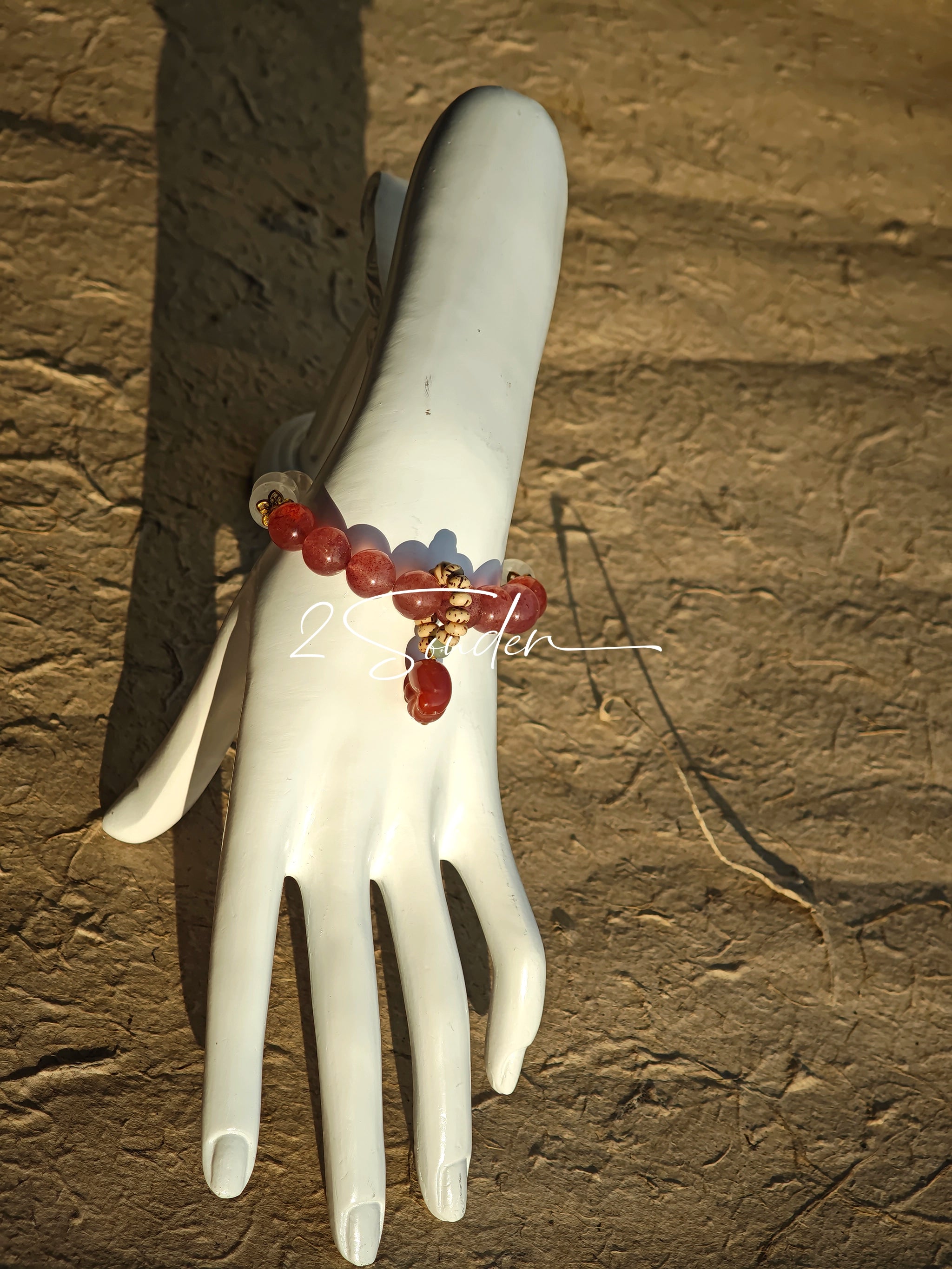 This bracelet features a beautiful blend of translucent white phantom quartz beads and rich pink strawberry quartz beads, creating a striking contrast. Adorned with delicate gold-toned accents and a charming red cat's paw charm, it exudes a sweet and elegant vibe. The combination of smooth crystal spheres and a playful pendant makes it a lovely and eye-catching accessory.