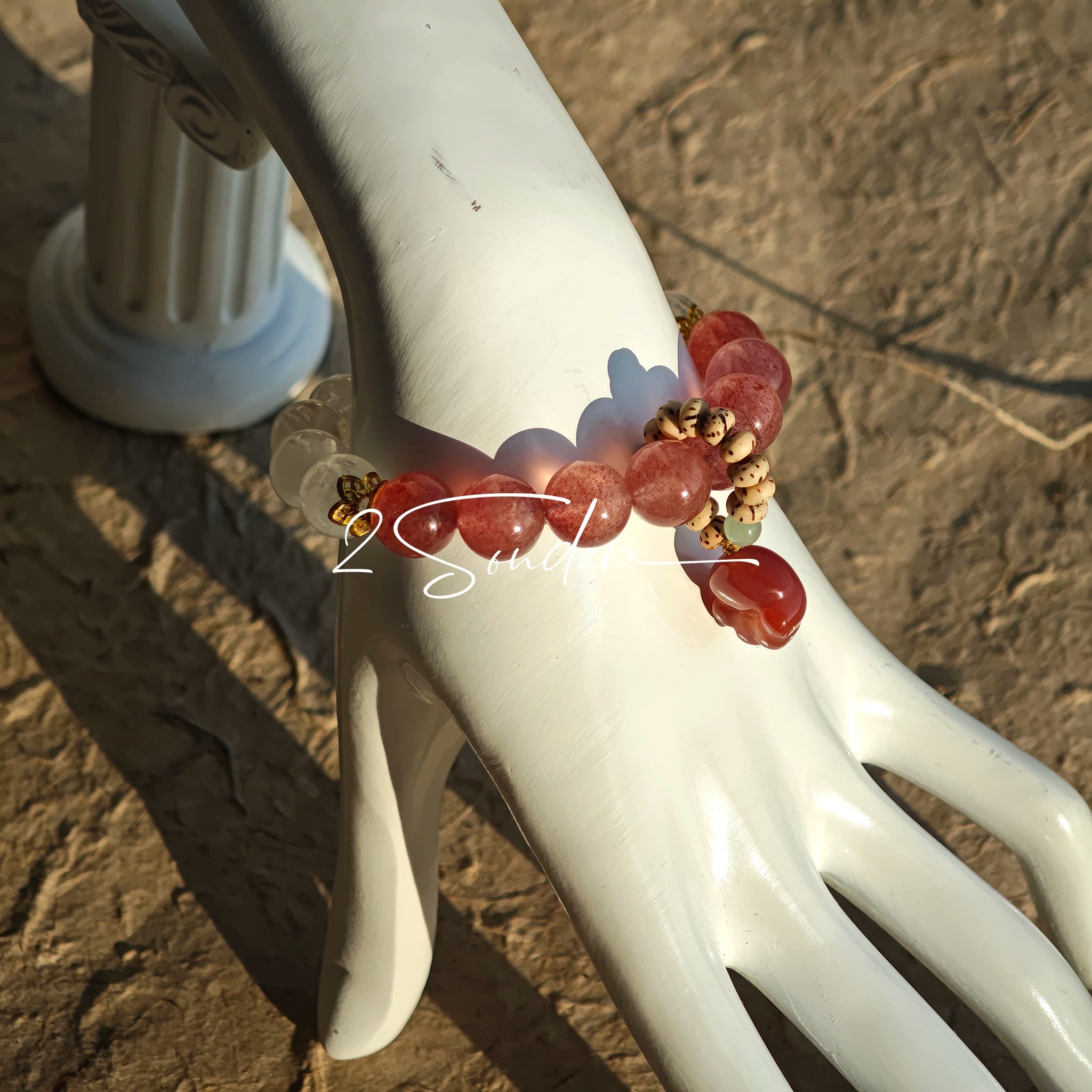 This bracelet features a beautiful blend of translucent white phantom quartz beads and rich pink strawberry quartz beads, creating a striking contrast. Adorned with delicate gold-toned accents and a charming red cat's paw charm, it exudes a sweet and elegant vibe. The combination of smooth crystal spheres and a playful pendant makes it a lovely and eye-catching accessory.