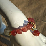 This bracelet features a beautiful blend of translucent white phantom quartz beads and rich pink strawberry quartz beads, creating a striking contrast. Adorned with delicate gold-toned accents and a charming red cat's paw charm, it exudes a sweet and elegant vibe. The combination of smooth crystal spheres and a playful pendant makes it a lovely and eye-catching accessory.