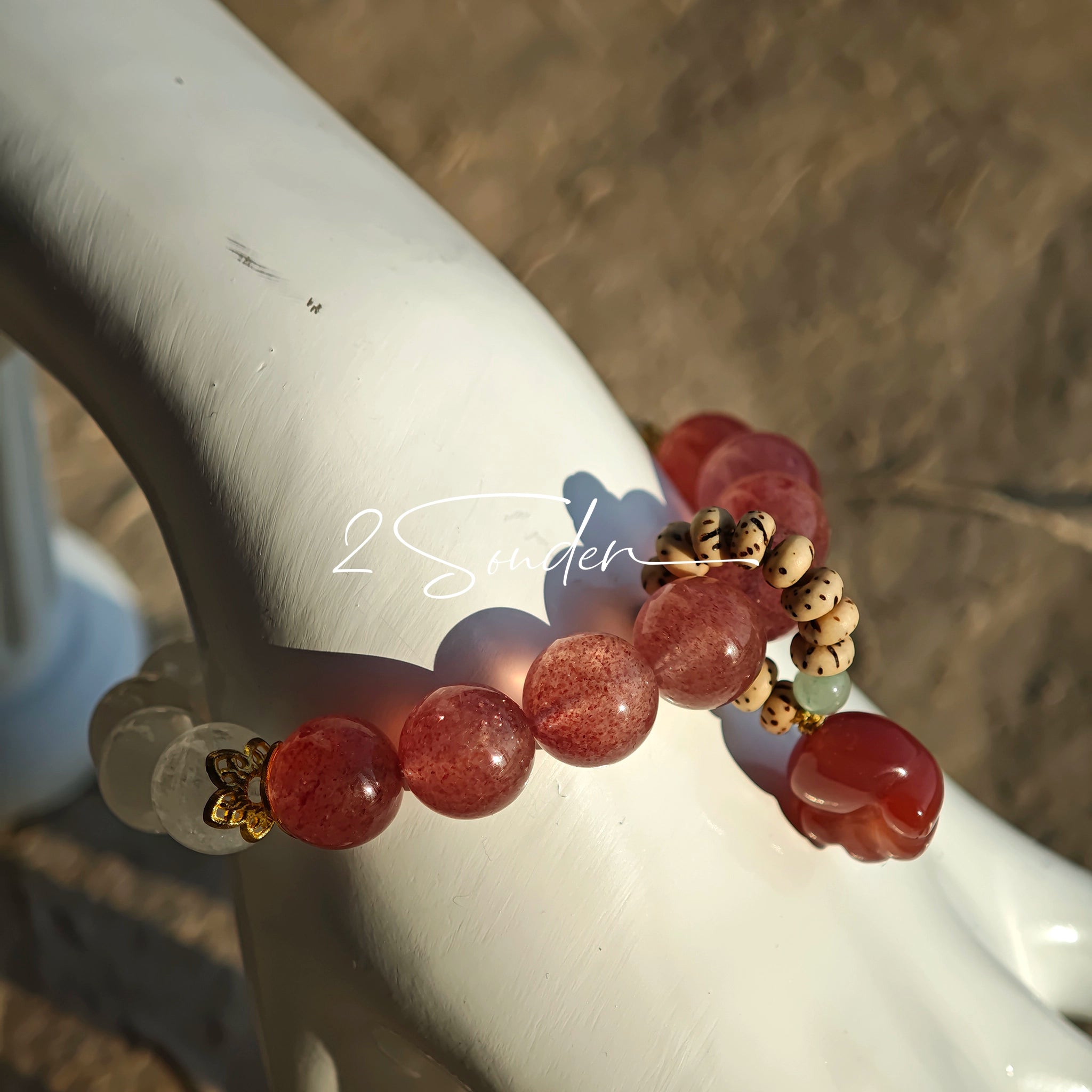 This bracelet features a beautiful blend of translucent white phantom quartz beads and rich pink strawberry quartz beads, creating a striking contrast. Adorned with delicate gold-toned accents and a charming red cat's paw charm, it exudes a sweet and elegant vibe. The combination of smooth crystal spheres and a playful pendant makes it a lovely and eye-catching accessory.