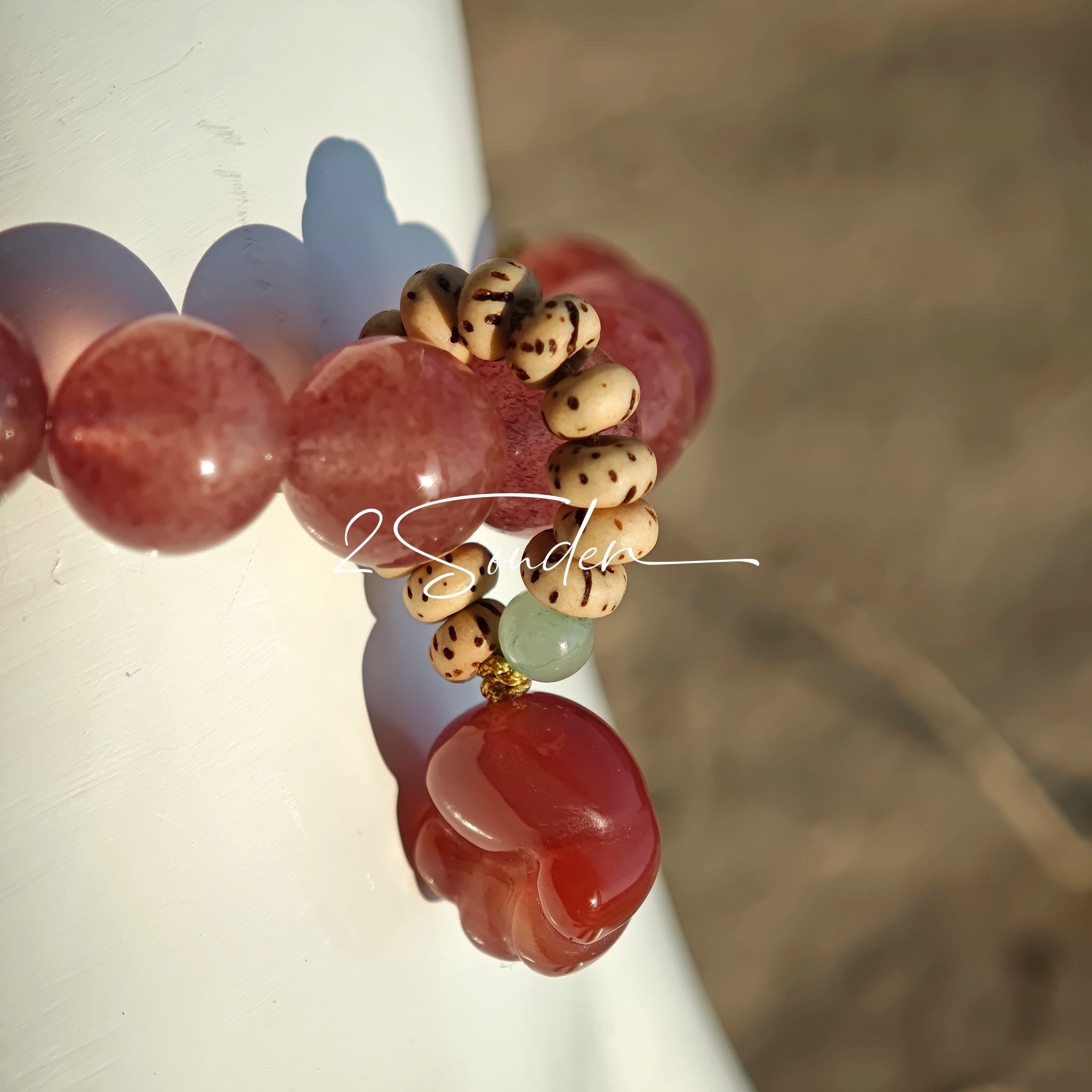 This bracelet features a beautiful blend of translucent white phantom quartz beads and rich pink strawberry quartz beads, creating a striking contrast. Adorned with delicate gold-toned accents and a charming red cat's paw charm, it exudes a sweet and elegant vibe. The combination of smooth crystal spheres and a playful pendant makes it a lovely and eye-catching accessory.