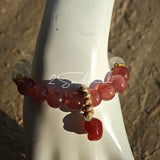 This bracelet features a beautiful blend of translucent white phantom quartz beads and rich pink strawberry quartz beads, creating a striking contrast. Adorned with delicate gold-toned accents and a charming red cat's paw charm, it exudes a sweet and elegant vibe. The combination of smooth crystal spheres and a playful pendant makes it a lovely and eye-catching accessory.