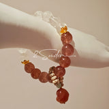 This bracelet features a beautiful blend of translucent white phantom quartz beads and rich pink strawberry quartz beads, creating a striking contrast. Adorned with delicate gold-toned accents and a charming red cat's paw charm, it exudes a sweet and elegant vibe. The combination of smooth crystal spheres and a playful pendant makes it a lovely and eye-catching accessory.