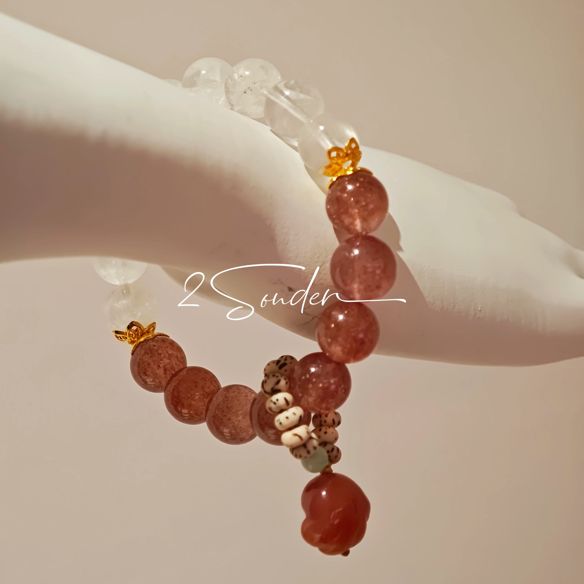 This bracelet features a beautiful blend of translucent white phantom quartz beads and rich pink strawberry quartz beads, creating a striking contrast. Adorned with delicate gold-toned accents and a charming red cat's paw charm, it exudes a sweet and elegant vibe. The combination of smooth crystal spheres and a playful pendant makes it a lovely and eye-catching accessory.
