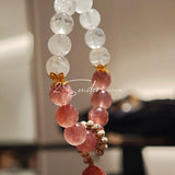 This bracelet features a beautiful blend of translucent white phantom quartz beads and rich pink strawberry quartz beads, creating a striking contrast. Adorned with delicate gold-toned accents and a charming red cat's paw charm, it exudes a sweet and elegant vibe. The combination of smooth crystal spheres and a playful pendant makes it a lovely and eye-catching accessory.