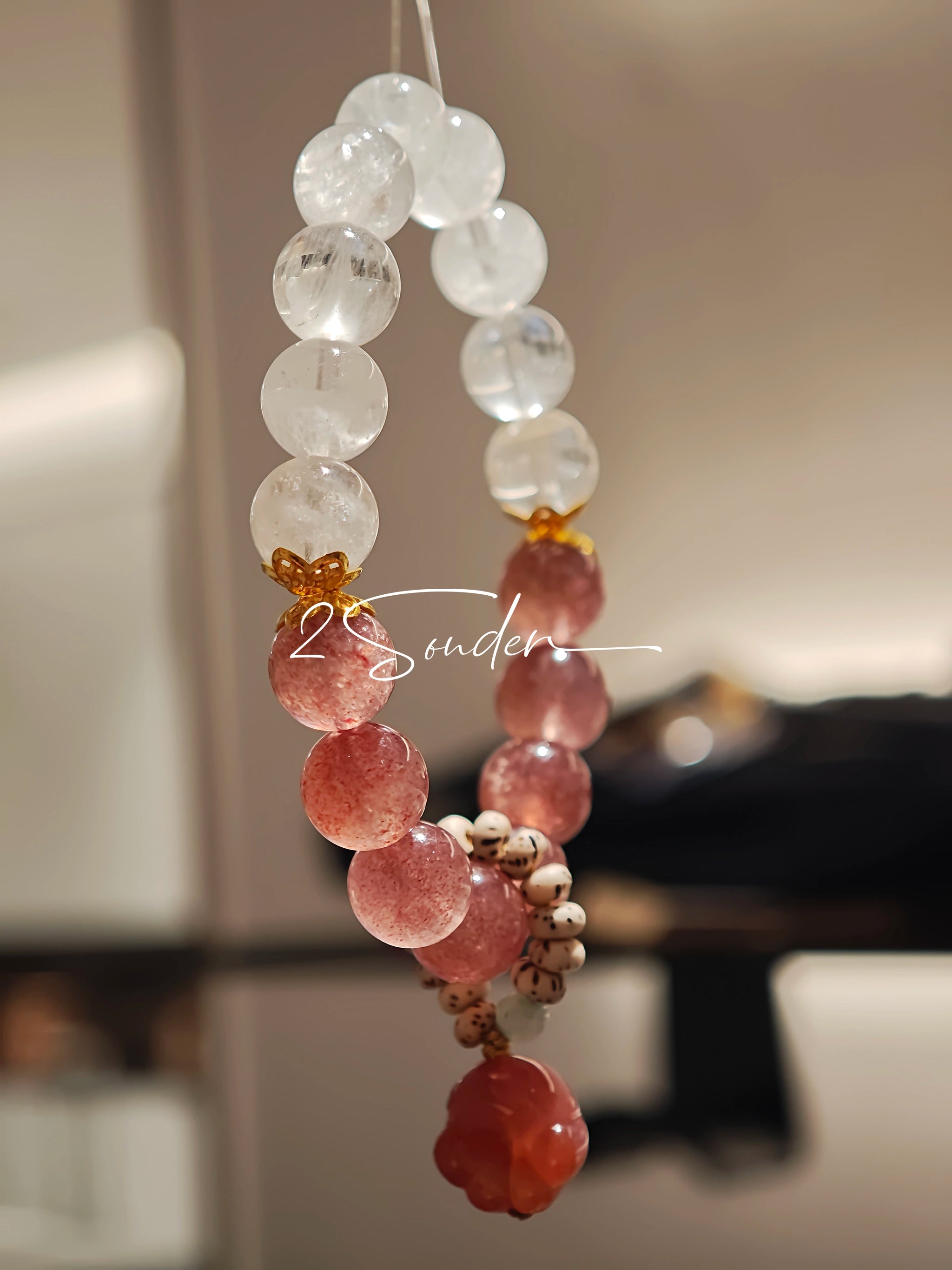 This bracelet features a beautiful blend of translucent white phantom quartz beads and rich pink strawberry quartz beads, creating a striking contrast. Adorned with delicate gold-toned accents and a charming red cat's paw charm, it exudes a sweet and elegant vibe. The combination of smooth crystal spheres and a playful pendant makes it a lovely and eye-catching accessory.