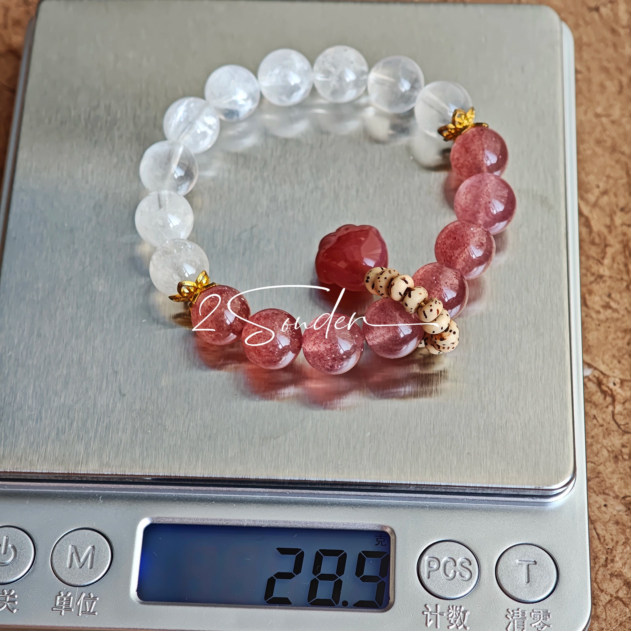 This bracelet features a beautiful blend of translucent white phantom quartz beads and rich pink strawberry quartz beads, creating a striking contrast. Adorned with delicate gold-toned accents and a charming red cat's paw charm, it exudes a sweet and elegant vibe. The combination of smooth crystal spheres and a playful pendant makes it a lovely and eye-catching accessory.