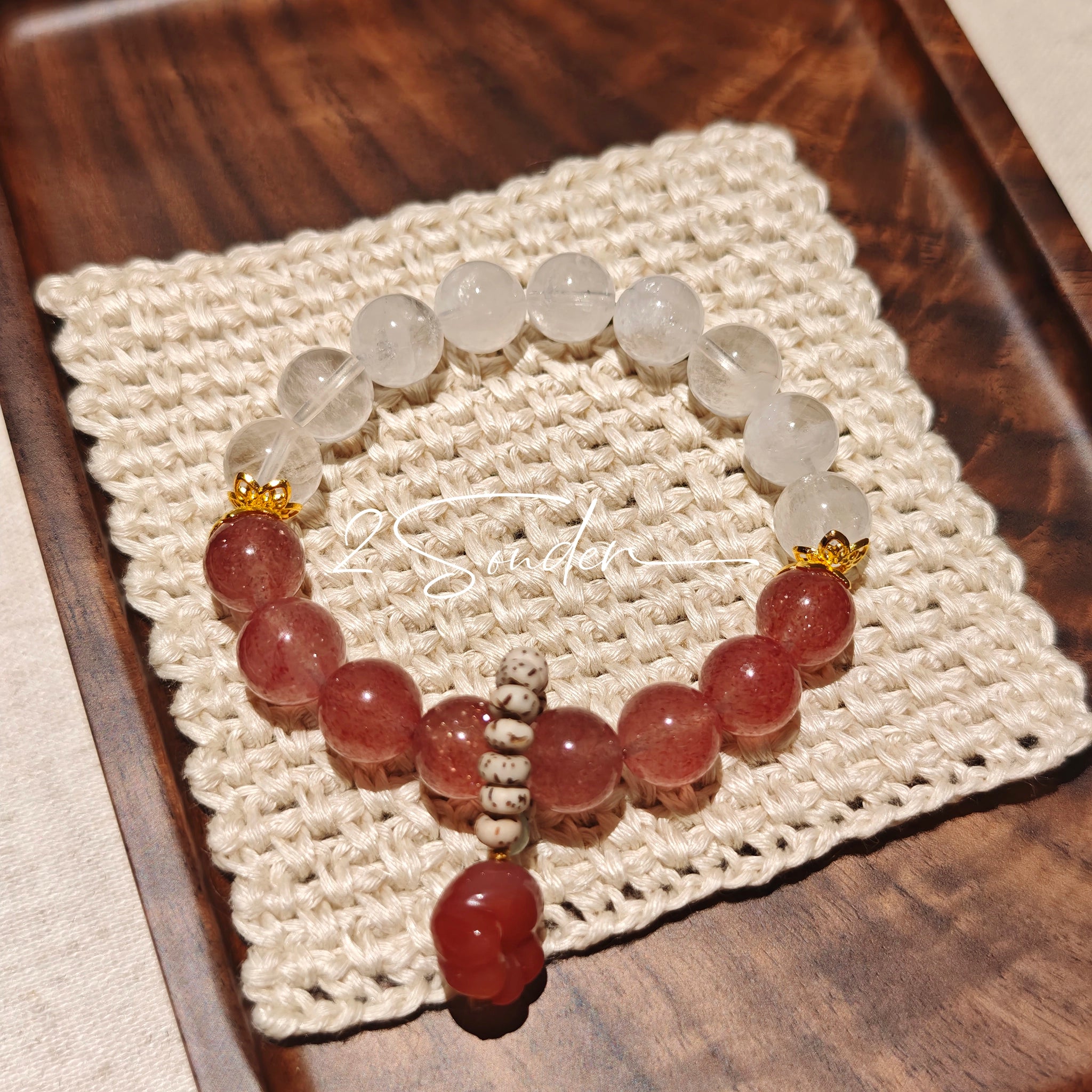 This bracelet features a beautiful blend of translucent white phantom quartz beads and rich pink strawberry quartz beads, creating a striking contrast. Adorned with delicate gold-toned accents and a charming red cat's paw charm, it exudes a sweet and elegant vibe. The combination of smooth crystal spheres and a playful pendant makes it a lovely and eye-catching accessory.