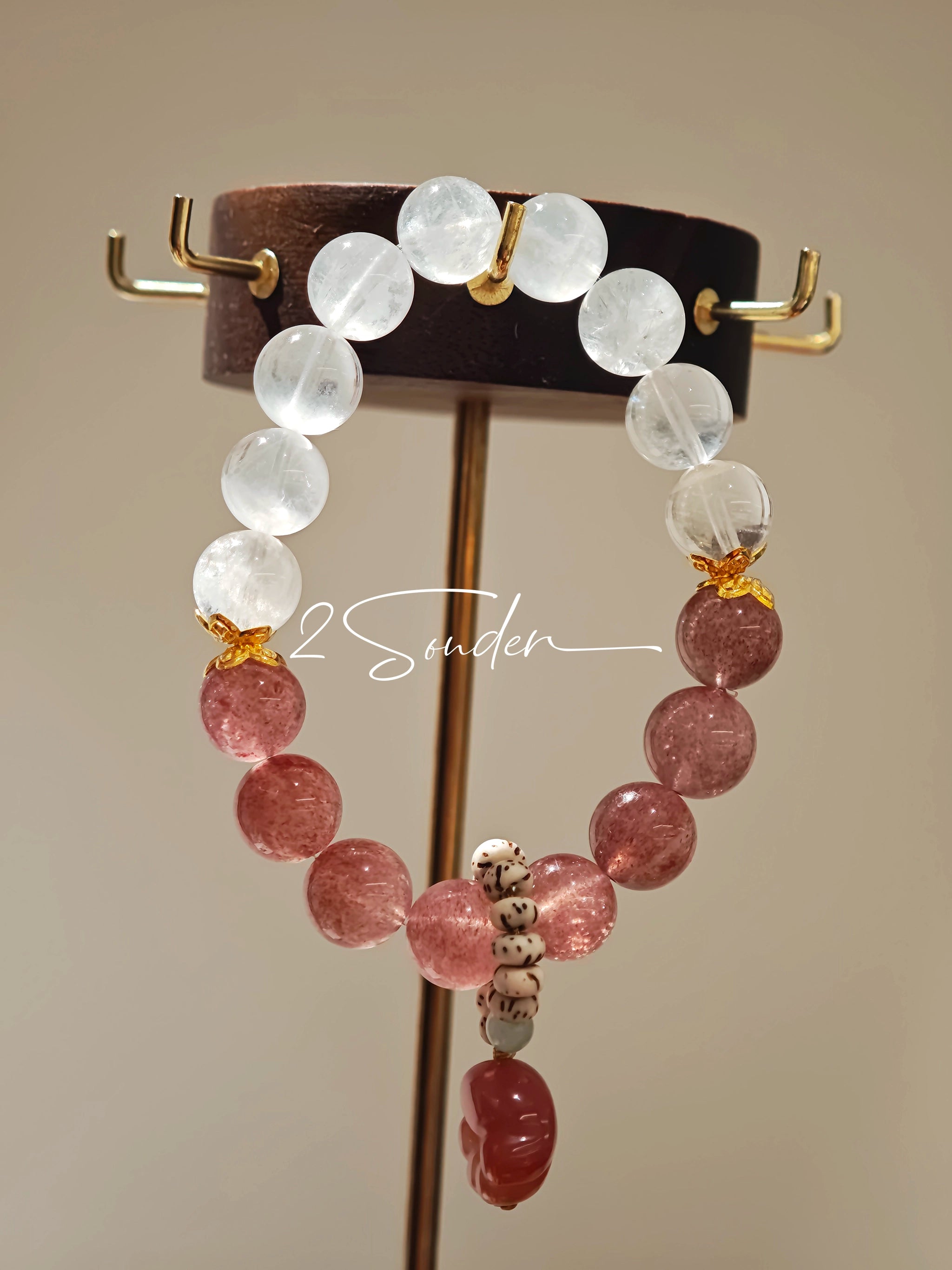 This bracelet features a beautiful blend of translucent white phantom quartz beads and rich pink strawberry quartz beads, creating a striking contrast. Adorned with delicate gold-toned accents and a charming red cat's paw charm, it exudes a sweet and elegant vibe. The combination of smooth crystal spheres and a playful pendant makes it a lovely and eye-catching accessory.