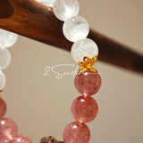 This bracelet features a beautiful blend of translucent white phantom quartz beads and rich pink strawberry quartz beads, creating a striking contrast. Adorned with delicate gold-toned accents and a charming red cat's paw charm, it exudes a sweet and elegant vibe. The combination of smooth crystal spheres and a playful pendant makes it a lovely and eye-catching accessory.