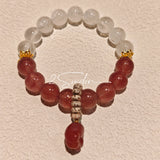 This bracelet features a beautiful blend of translucent white phantom quartz beads and rich pink strawberry quartz beads, creating a striking contrast. Adorned with delicate gold-toned accents and a charming red cat's paw charm, it exudes a sweet and elegant vibe. The combination of smooth crystal spheres and a playful pendant makes it a lovely and eye-catching accessory.