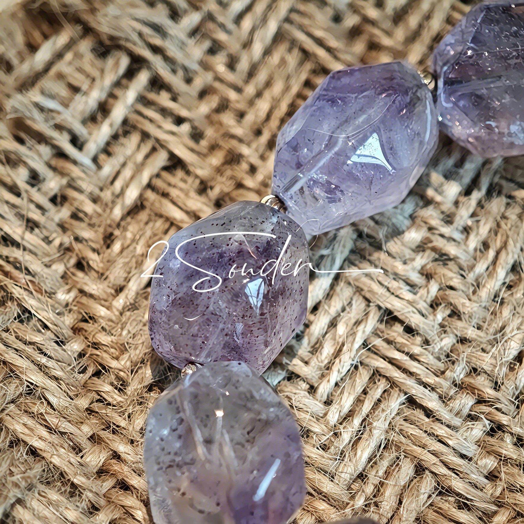 This exquisite Super Seven bracelet showcases irregularly faceted beads in a captivating blend of soft lavender and smoky purple hues, each displaying unique natural inclusions that catch the light beautifully. The polished crystals are seamlessly interspersed with tiny metallic spacer beads, culminating in an ornate silver-tone decorative bead that adds a touch of elegance to the organic design. Crafted with meticulous attention to detail, the bracelet offers a harmonious blend of rare gemstone texture and