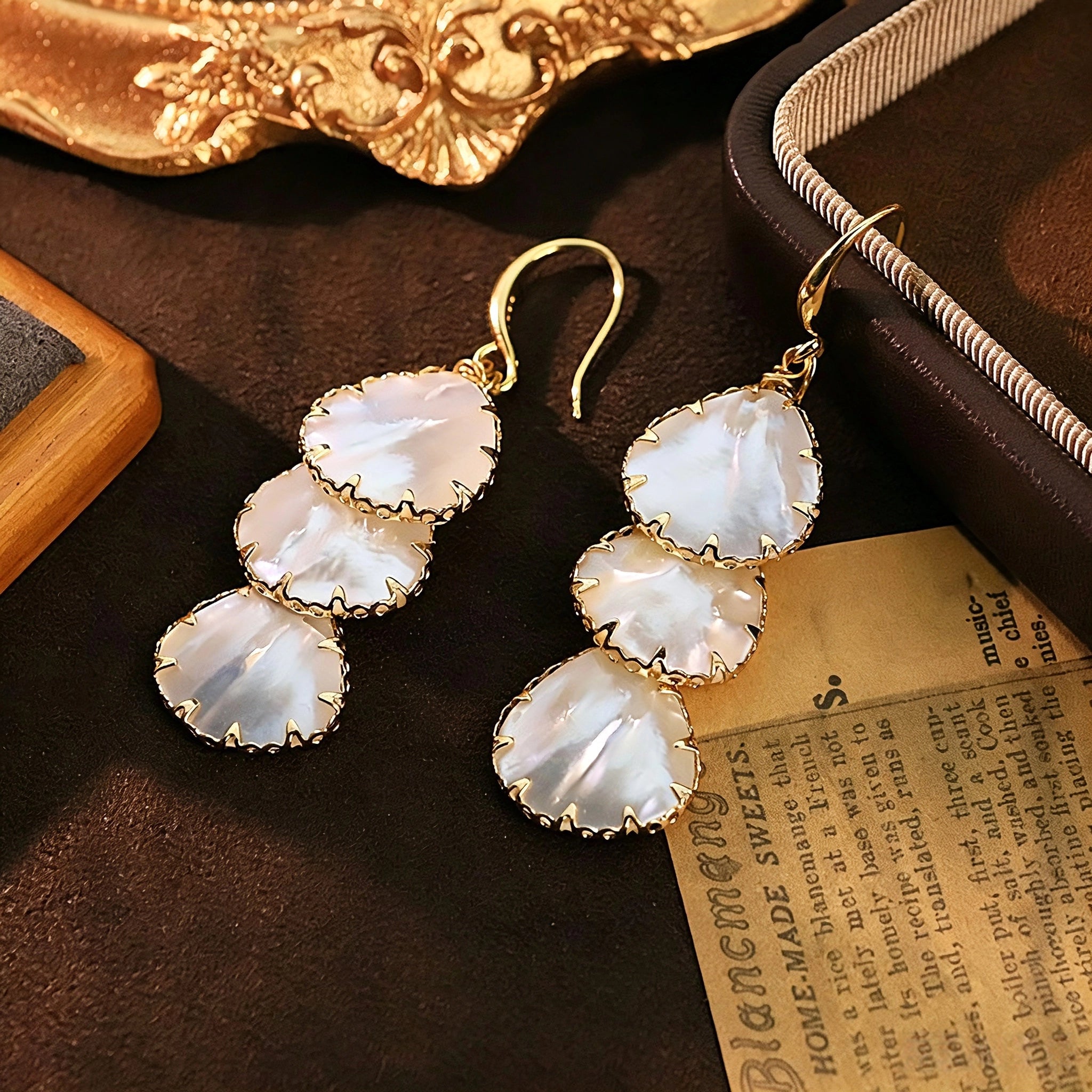 These drop earrings feature three layered natural shell slices with iridescent pearlescent luster. Each shell piece is framed by delicate gold‑tone metal trim for a vintage elegant look. The hook design offers comfortable wear for everyday and special occasions.
