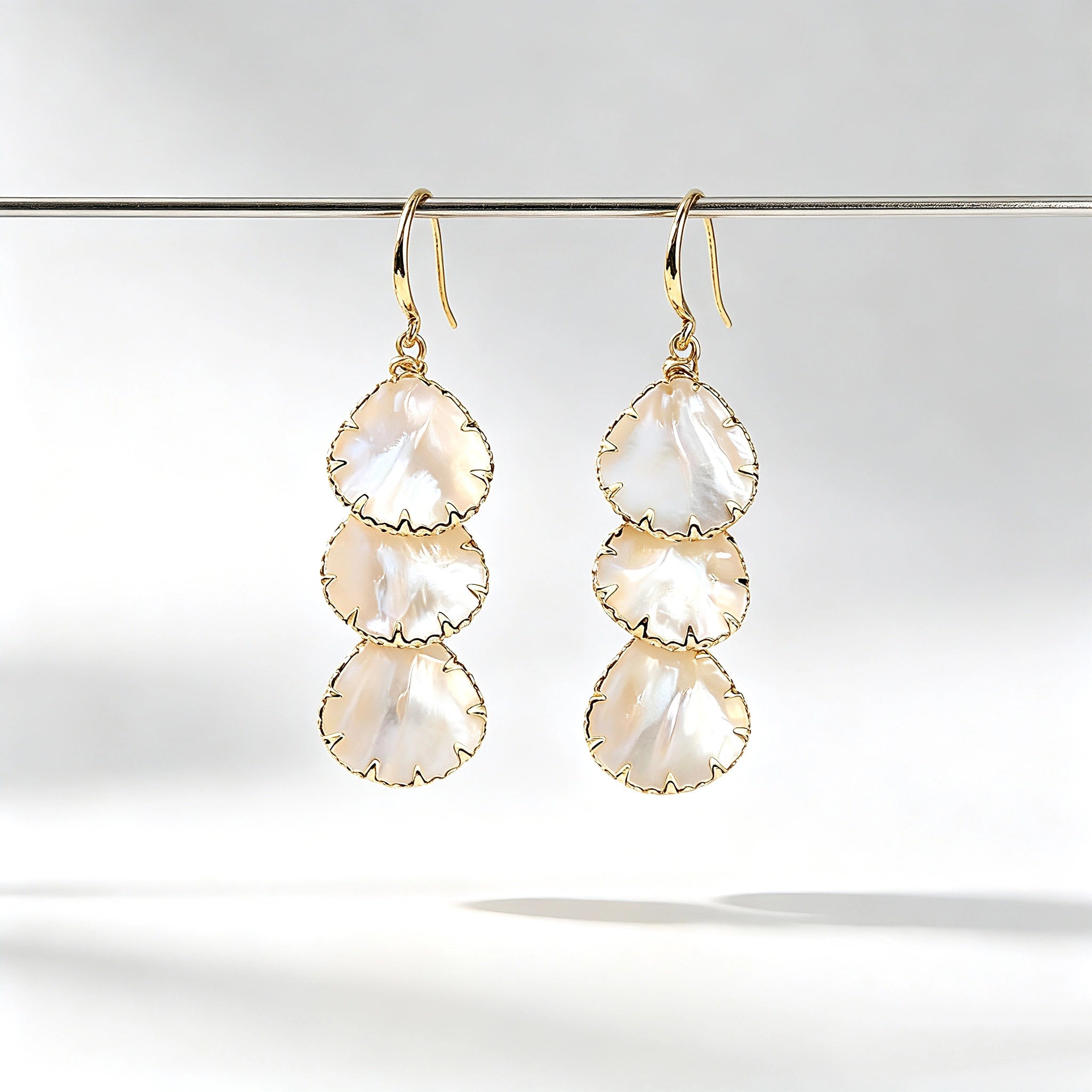 These drop earrings feature three layered natural shell slices with iridescent pearlescent luster. Each shell piece is framed by delicate gold‑tone metal trim for a vintage elegant look. The hook design offers comfortable wear for everyday and special occasions.