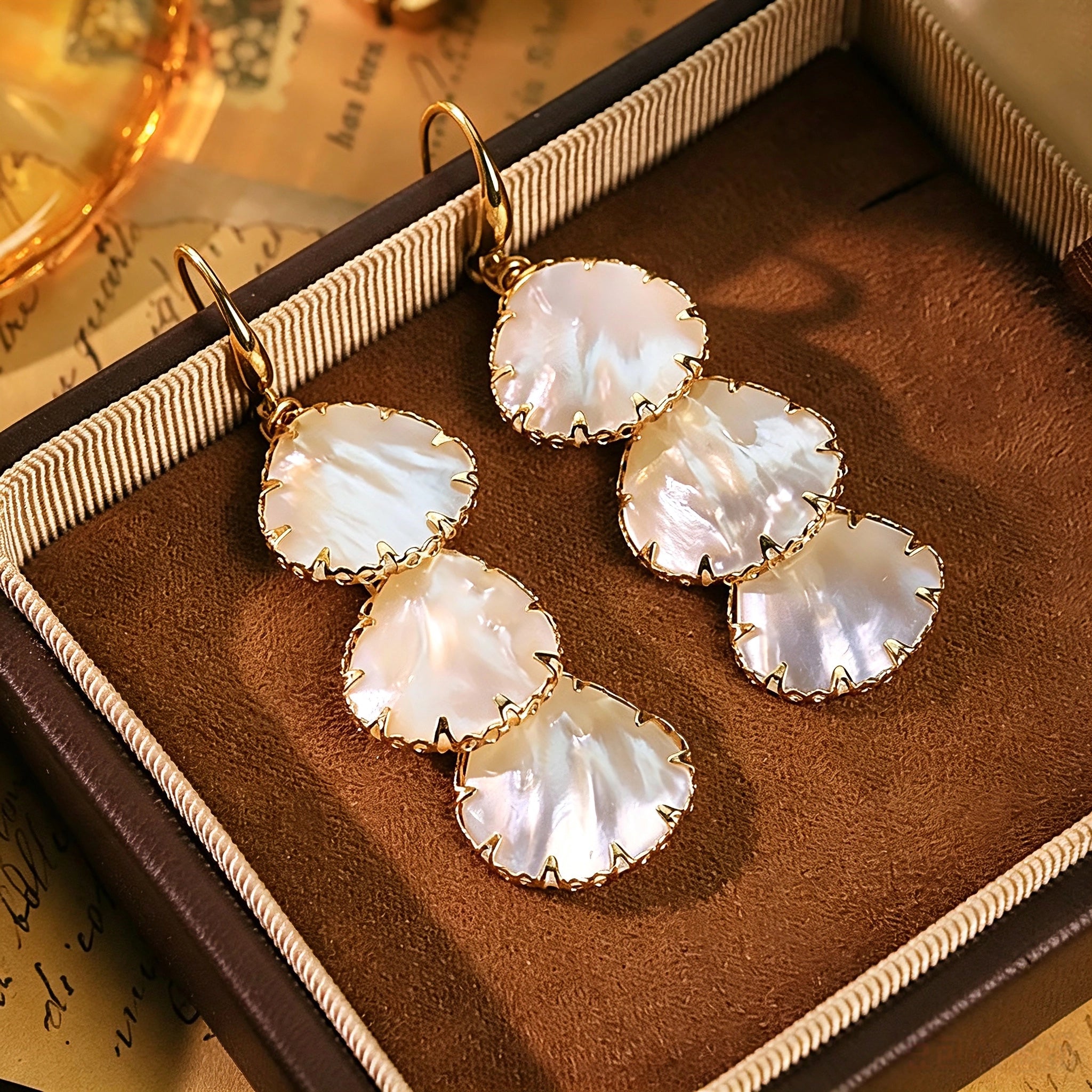 These drop earrings feature three layered natural shell slices with iridescent pearlescent luster. Each shell piece is framed by delicate gold‑tone metal trim for a vintage elegant look. The hook design offers comfortable wear for everyday and special occasions.