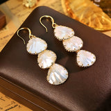 These drop earrings feature three layered natural shell slices with iridescent pearlescent luster. Each shell piece is framed by delicate gold‑tone metal trim for a vintage elegant look. The hook design offers comfortable wear for everyday and special occasions.