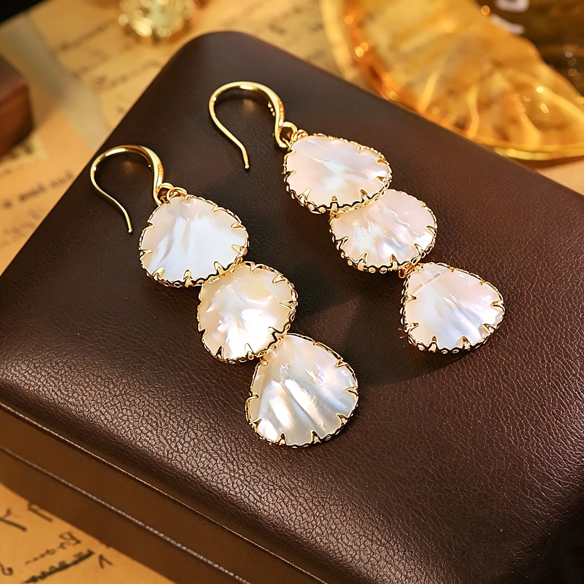These drop earrings feature three layered natural shell slices with iridescent pearlescent luster. Each shell piece is framed by delicate gold‑tone metal trim for a vintage elegant look. The hook design offers comfortable wear for everyday and special occasions.