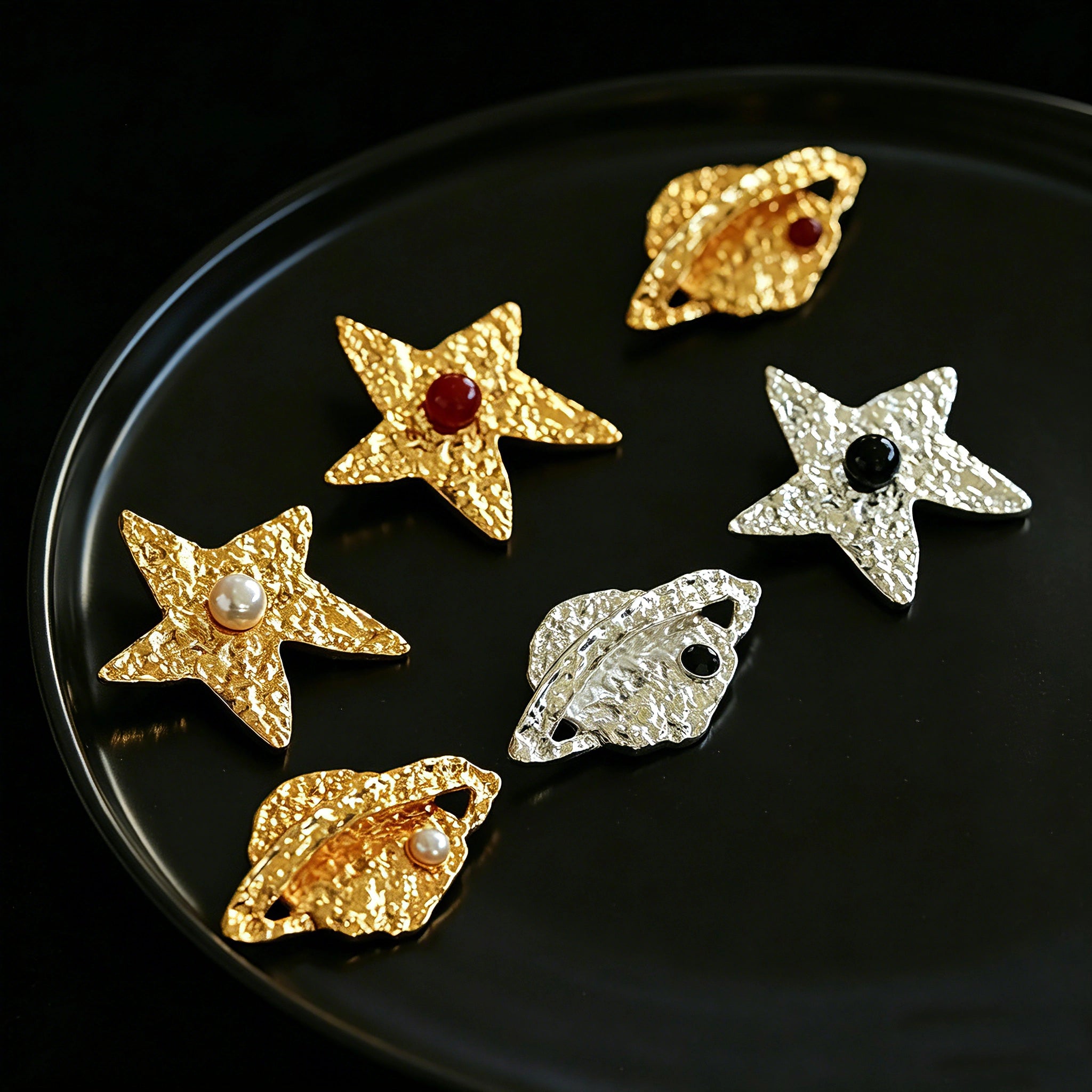 These vintage-style brooches come in star and Saturn-inspired planet shapes, with a hammered, textured finish in gold or silver tone. Each design is accented with a central gemstone, including pearl, red agate, or black onyx, adding a touch of celestial charm to any outfit.
