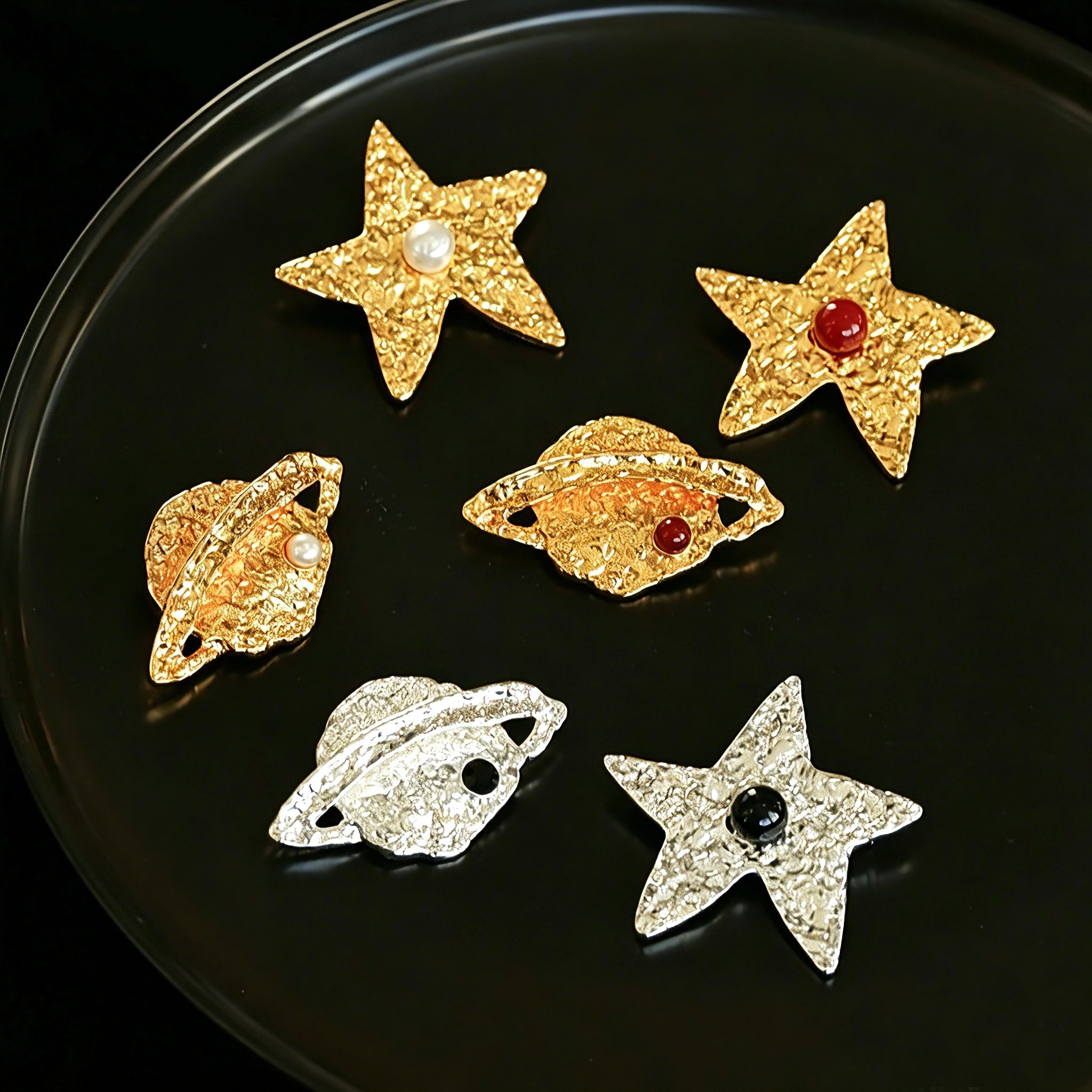 These vintage-style brooches come in star and Saturn-inspired planet shapes, with a hammered, textured finish in gold or silver tone. Each design is accented with a central gemstone, including pearl, red agate, or black onyx, adding a touch of celestial charm to any outfit.
