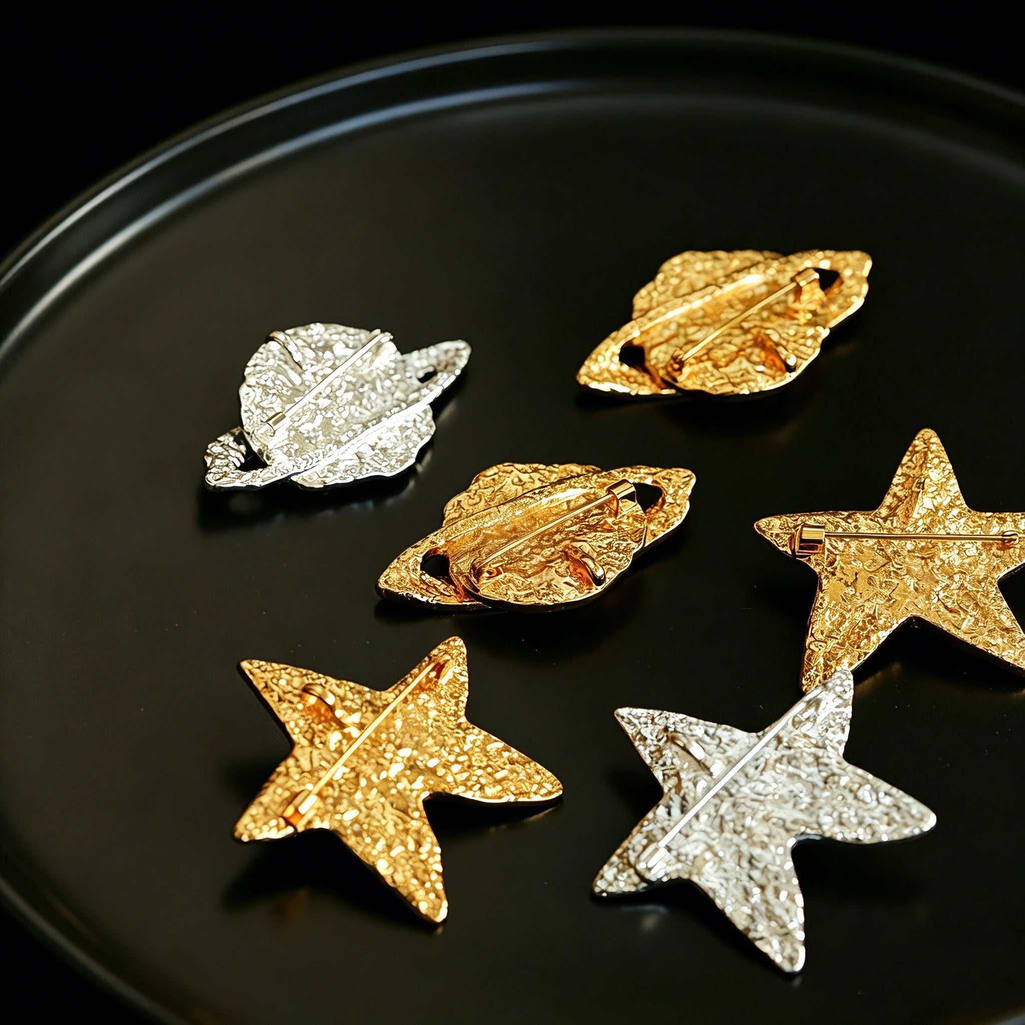 These vintage-style brooches come in star and Saturn-inspired planet shapes, with a hammered, textured finish in gold or silver tone. Each design is accented with a central gemstone, including pearl, red agate, or black onyx, adding a touch of celestial charm to any outfit.