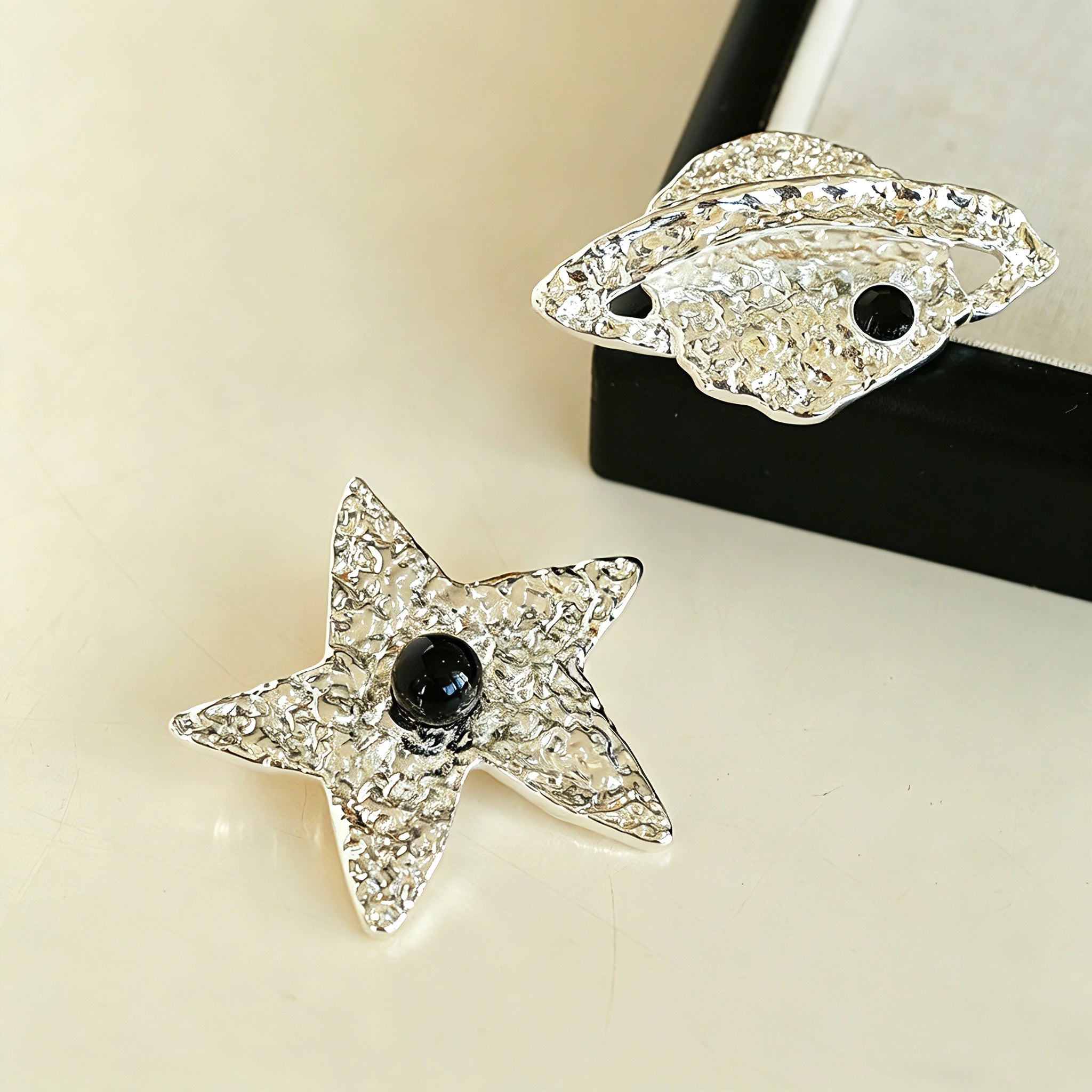 These vintage-style brooches come in star and Saturn-inspired planet shapes, with a hammered, textured finish in gold or silver tone. Each design is accented with a central gemstone, including pearl, red agate, or black onyx, adding a touch of celestial charm to any outfit.