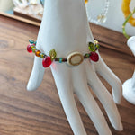This vibrant bracelet features a colorful mix of ruby-red lemon, sapphire-blue flower, and emerald-green leaf charms, all dangling from a shimmering Czech glass bead chain.