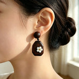 Crafted from vintage‑style dark wood, these drop earrings feature delicate small white flower accents with golden centers. Natural wood grain brings warm retro texture, suspended by black knotted cord for a soft boho‑charm look. They are lightweight statement pieces perfect for daily and casual styling.
