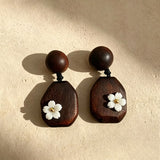 Crafted from vintage‑style dark wood, these drop earrings feature delicate small white flower accents with golden centers. Natural wood grain brings warm retro texture, suspended by black knotted cord for a soft boho‑charm look. They are lightweight statement pieces perfect for daily and casual styling.