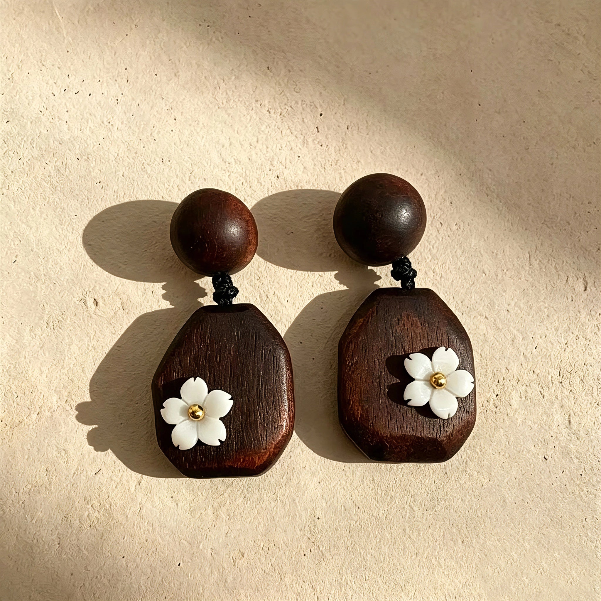 Crafted from vintage‑style dark wood, these drop earrings feature delicate small white flower accents with golden centers. Natural wood grain brings warm retro texture, suspended by black knotted cord for a soft boho‑charm look. They are lightweight statement pieces perfect for daily and casual styling.