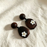 Crafted from vintage‑style dark wood, these drop earrings feature delicate small white flower accents with golden centers. Natural wood grain brings warm retro texture, suspended by black knotted cord for a soft boho‑charm look. They are lightweight statement pieces perfect for daily and casual styling.