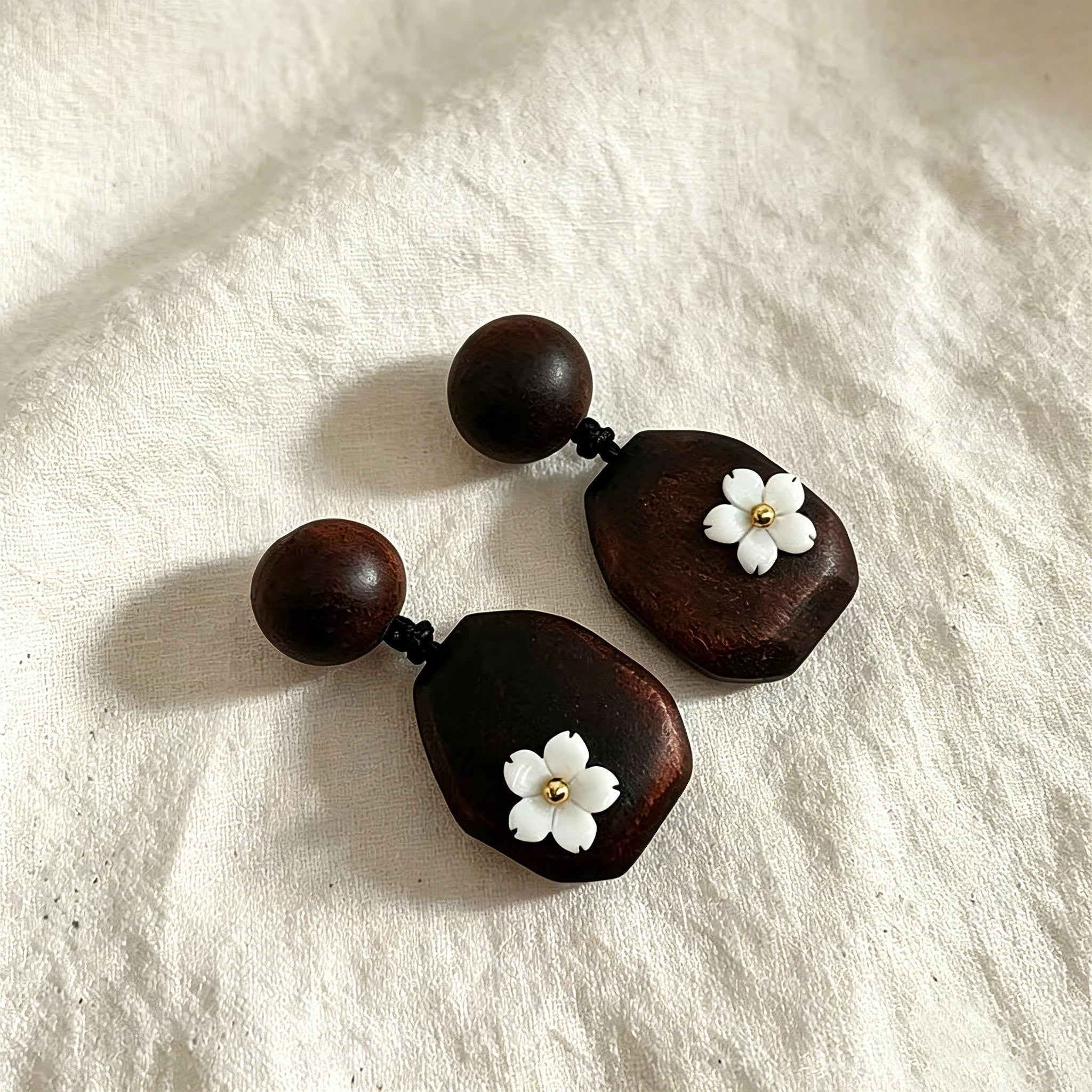 Crafted from vintage‑style dark wood, these drop earrings feature delicate small white flower accents with golden centers. Natural wood grain brings warm retro texture, suspended by black knotted cord for a soft boho‑charm look. They are lightweight statement pieces perfect for daily and casual styling.