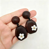 Crafted from vintage‑style dark wood, these drop earrings feature delicate small white flower accents with golden centers. Natural wood grain brings warm retro texture, suspended by black knotted cord for a soft boho‑charm look. They are lightweight statement pieces perfect for daily and casual styling.