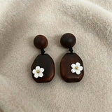 Crafted from vintage‑style dark wood, these drop earrings feature delicate small white flower accents with golden centers. Natural wood grain brings warm retro texture, suspended by black knotted cord for a soft boho‑charm look. They are lightweight statement pieces perfect for daily and casual styling.