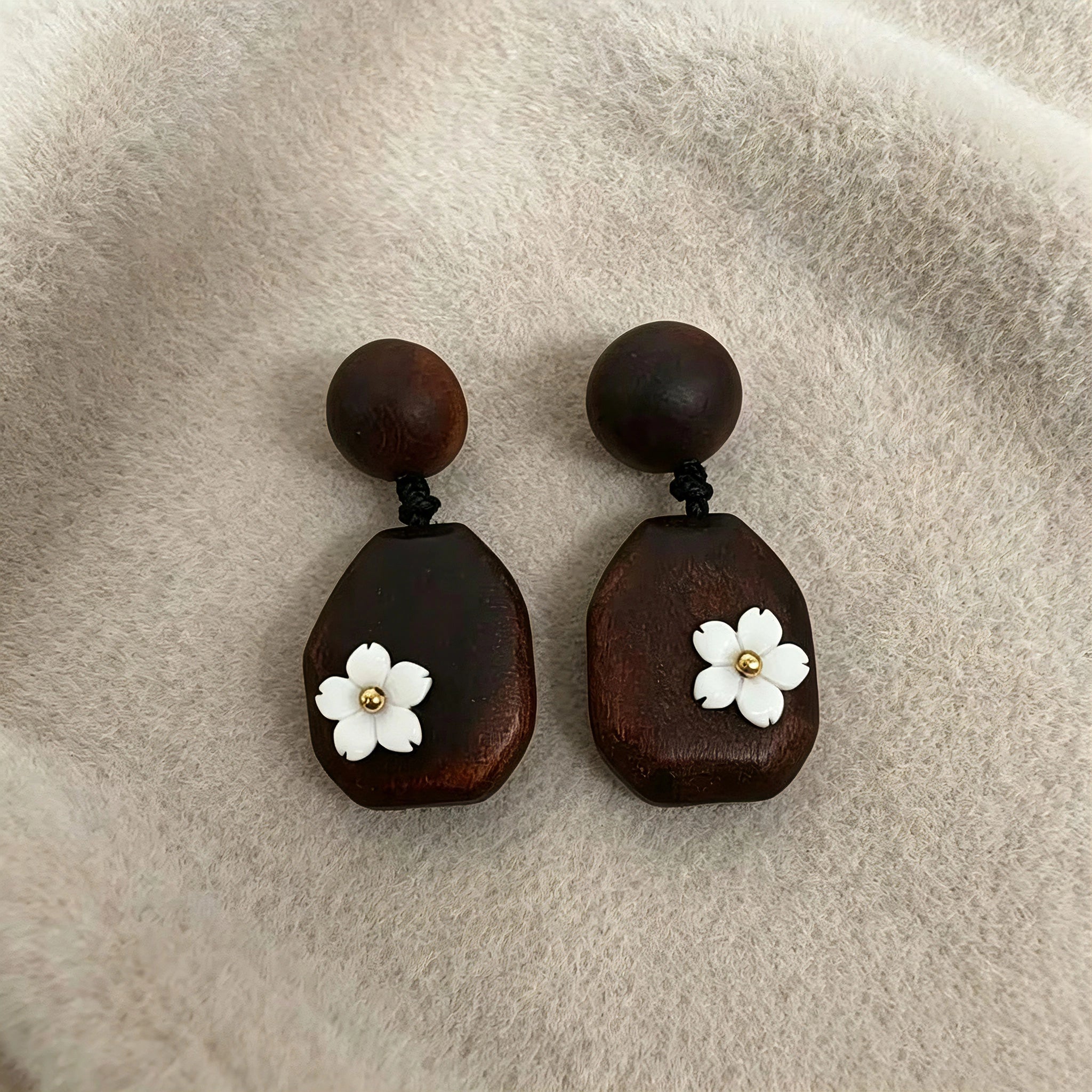 Crafted from vintage‑style dark wood, these drop earrings feature delicate small white flower accents with golden centers. Natural wood grain brings warm retro texture, suspended by black knotted cord for a soft boho‑charm look. They are lightweight statement pieces perfect for daily and casual styling.
