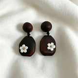 Crafted from vintage‑style dark wood, these drop earrings feature delicate small white flower accents with golden centers. Natural wood grain brings warm retro texture, suspended by black knotted cord for a soft boho‑charm look. They are lightweight statement pieces perfect for daily and casual styling.