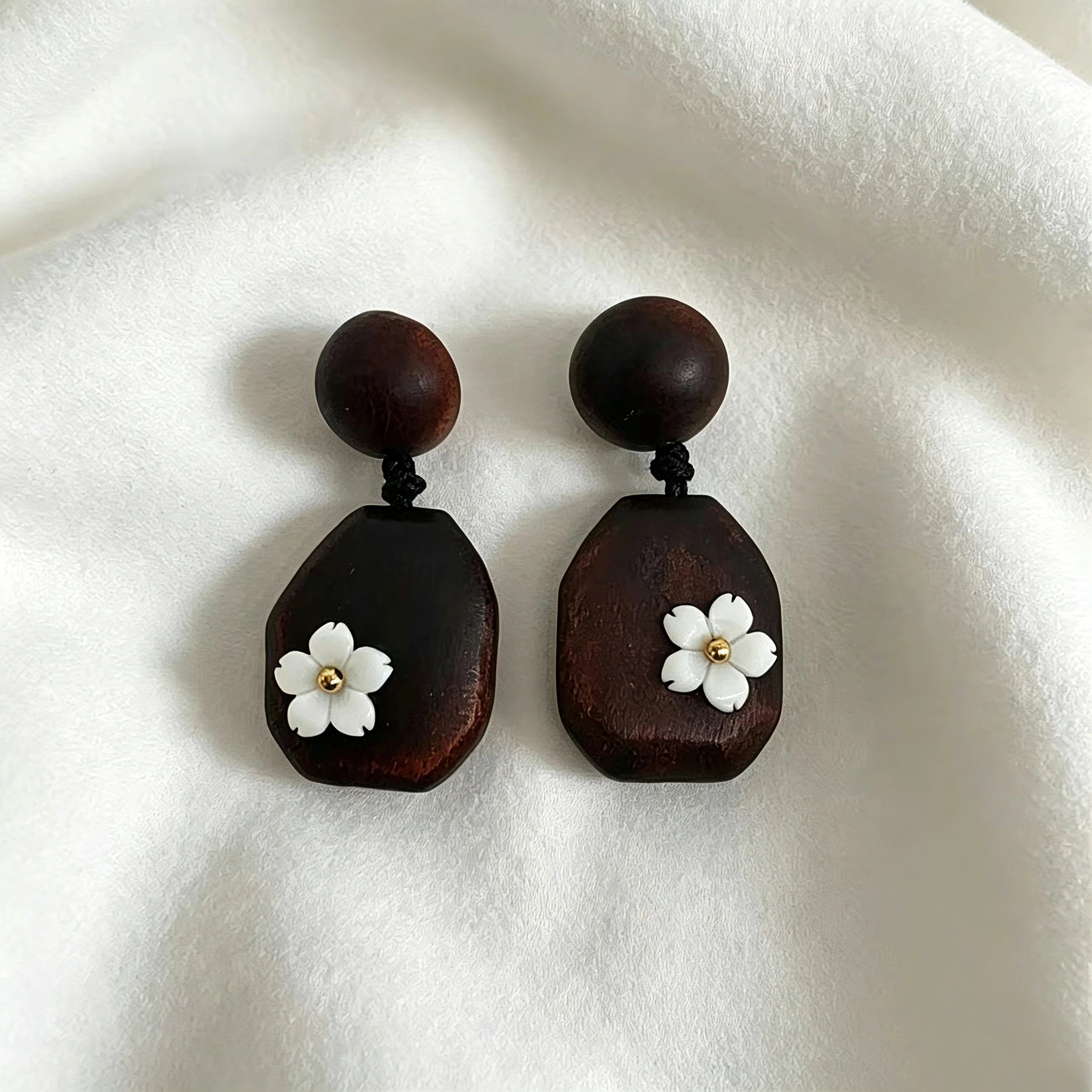 Crafted from vintage‑style dark wood, these drop earrings feature delicate small white flower accents with golden centers. Natural wood grain brings warm retro texture, suspended by black knotted cord for a soft boho‑charm look. They are lightweight statement pieces perfect for daily and casual styling.