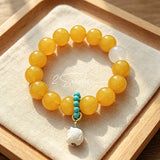 This handcrafted bracelet features glossy 14mm yellow agate beads paired with one white agate bead. It is accented with turquoise beads and finished with a detailed mammoth ivory guardian lion charm, bringing a warm vintage ethnic vibe.