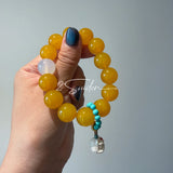 This handcrafted bracelet features glossy 14mm yellow agate beads paired with one white agate bead. It is accented with turquoise beads and finished with a detailed mammoth ivory guardian lion charm, bringing a warm vintage ethnic vibe.