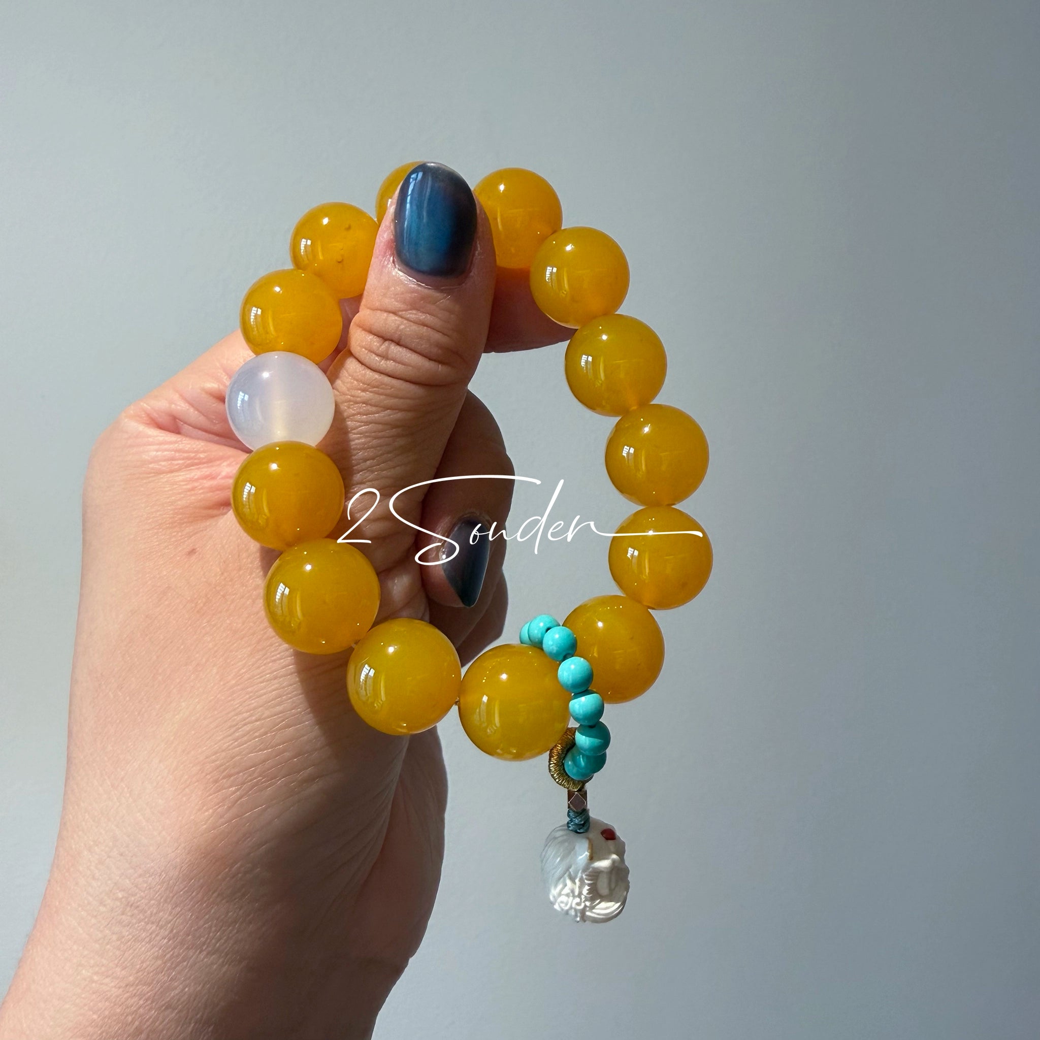 This handcrafted bracelet features glossy 14mm yellow agate beads paired with one white agate bead. It is accented with turquoise beads and finished with a detailed mammoth ivory guardian lion charm, bringing a warm vintage ethnic vibe.